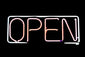 Neon 'OPEN' sign glowing in pink and blue on a dark background and RAND HOME written smaller above the word open